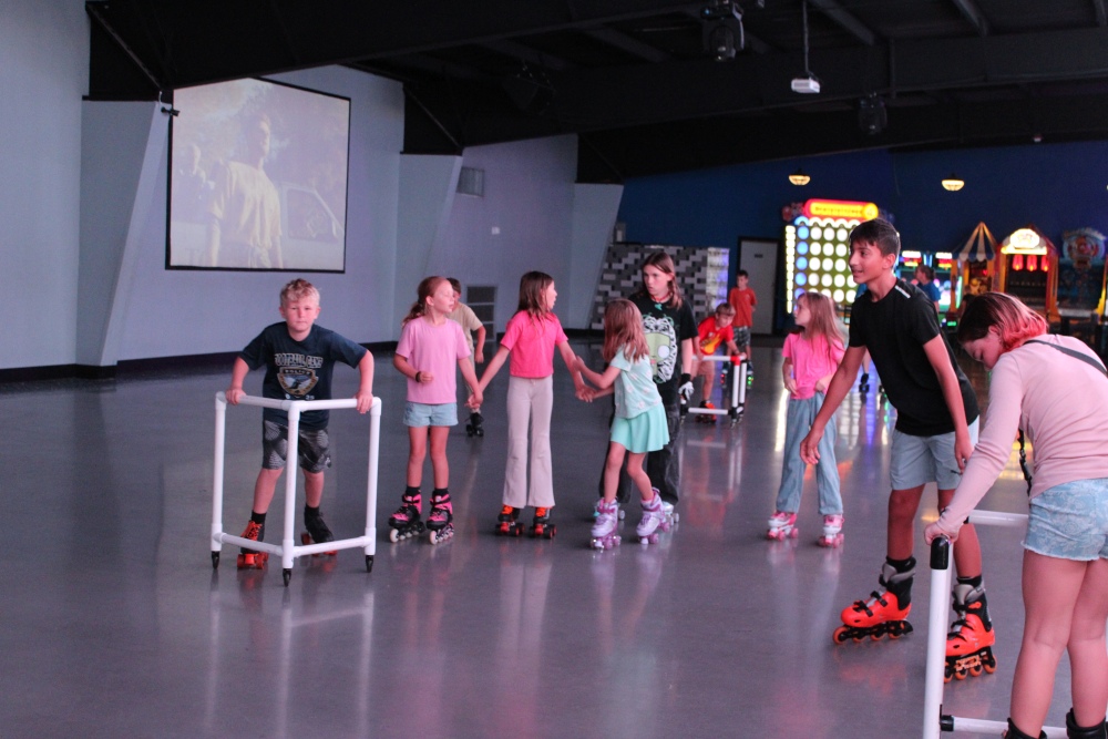 Kids in roller skates practice together on an indoor rink with arcade games in the background